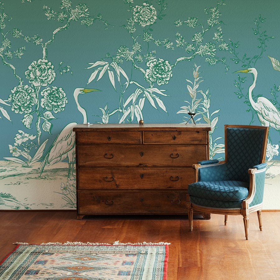 Elegant green heron mural wallpaper with floral design, featuring vintage wooden chest, blue armchair, rug.