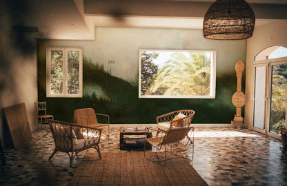 Elegant lounge with Tranquil Misty Forest Landscape Mural, wicker furniture, tiled flooring, serene greenery.